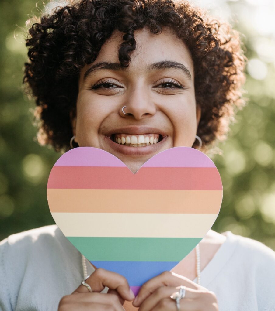 Woman holding a heart shape rainbow paper, smiling.